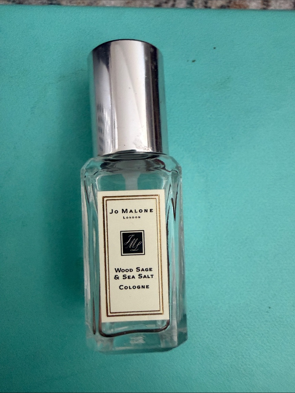 Jo Malone clear bottle with silver cap on teal background